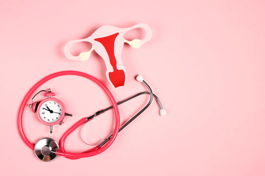 Paper cutout of a uterus beside a pink alarm clock and stethoscope on a pink background, symbolizing the hormonal transition of perimenopause